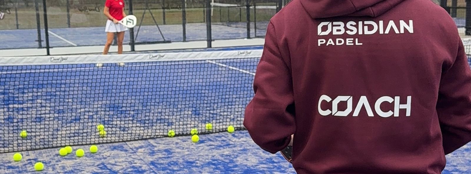 A coach in the Obsidian Padel hoodie on a blue padel court.